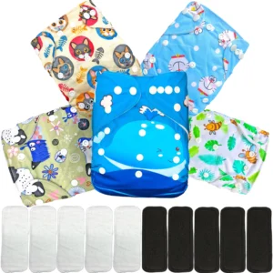 Kit de pañales ecológicos reutilizables de tela unisex para bebé. Incluye 5 pañales lavables con estampados coloridos (una ballena azul al centro, gatos con espinas de pescado, gatos tipo anime, abejitas con hojas verdes y monstruos tiernos). En la parte inferior se muestran 5 insertos absorbentes blancos y 5 insertos negros de carbón de bambú.