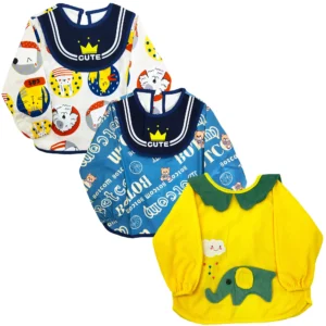 Tres baberos de manga larga tipo bata para bebé en color blanco con figuras, azul con letras y amarillo con un elefante verde, mostrados sobre fondo blanco.