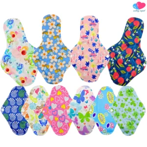 Catálogo de toallas femeninas de tela reutilizables sobre fondo blanco limpio. En la fila superior se muestran 4 toallas nocturnas más largas con estampados de remolinos de colores, abejas con flores, camaleones rosados y naranjas con hojas. En la fila inferior hay 6 toallas regulares con patrones de abanicos azules, flores con mariposas, corazones rosas, mariposas grandes, hojas abstractas y tréboles verdes. En la esquina superior derecha se incluye el logotipo de "ecobaby original". El archivo de referencia es 4 toallas nocturnas 6 regulares pads